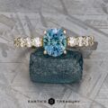 The "Juno" ring in 14k yellow gold showcases a striking 1.54-carat round Montana sapphire, accented by small sparkling stones, beautifully displayed on a rugged blue mineral.