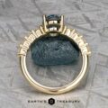 The "Juno" ring in 14k yellow gold, featuring a large 1.54-carat Montana sapphire solitaire gemstone at its center, rests on a textured metallic surface.
