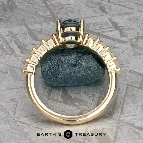 The "Juno" ring in 14k yellow gold with 1.54-carat Montana sapph The "Juno" ring in 14k yellow gold, featuring a large 1.54-carat Montana sapphire solitaire gemstone at its center, rests on a textured metallic surface.