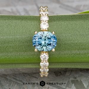The "Juno" ring, crafted in 14k yellow gold and featuring a 1.54-carat Montana sapphire, is elegantly displayed on a green leaf with its diamond-accented details.