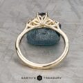 The Estes, Kayley and Nore, Caroline 1 ring features an intricate gold trellis cluster design around a dark gemstone, displayed upright on a textured gray surface with "EARTH'S TREASURY" at the bottom.