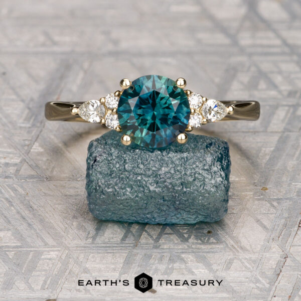 The "Arwyn" ring in 14K yellow gold with 1.80-carat Montana sapphire The "Arwyn" ring in 14K yellow gold, featuring a 1.80-carat Montana sapphire and side diamonds, is displayed upright on a rough blue-green stone.