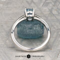 The Cathedral "Lyra" ring in platinum with a 1.44-carat Montana sapphire rests atop a rough blue stone on a textured gray surface, with "Earth's Treasury" labeled at the bottom.