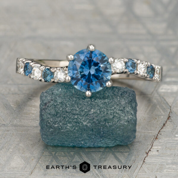 The "Halia" ring in 14K white gold with 1.12-carat Montana sapphire The "Halia" ring in 14K white gold with a 1.12-carat Montana sapphire is displayed upright on a rough blue stone; Earth's Treasury logo appears at the bottom.