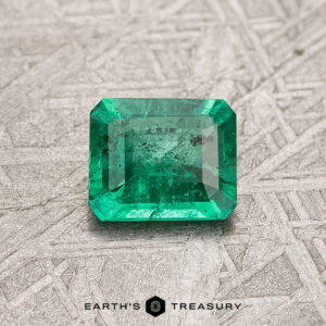 A 0.53-carat Colombian emerald, enhanced through treatment and showcasing visible inclusions, rests on a textured surface, its vibrant green hue captivating the eye.