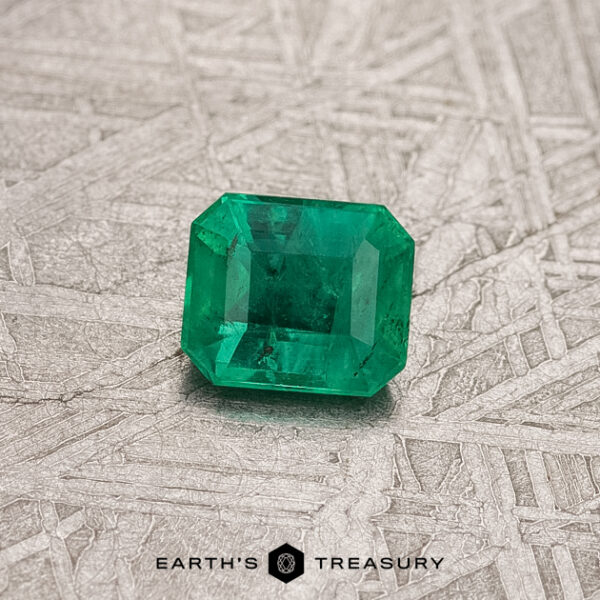 0.37-Carat Colombian Emerald (Treated) The 0.37-Carat Colombian Emerald (Treated), a vibrant green gem from Colombia, is elegantly showcased on a textured gray surface.