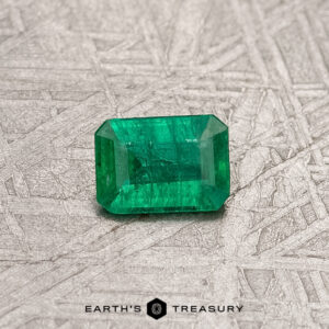 A breathtaking 0.28-carat treated Colombian emerald with a radiant green hue elegantly adorns a textured gray surface, captivating the eye.