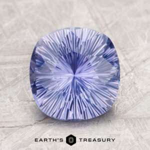 A cushion-cut, radiant blue-purple gemstone displayed on a textured surface, labeled as "2.60-Carat Ceylon Sapphire" by Earth's Treasury below it.