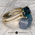The "Gaia" ring in 14k yellow gold, featuring a 4.63-carat Montana sapphire and diamond-studded band, rests on a rough stone with the Earth's Treasury logo below.
