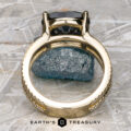 The "Gaia" ring in 14k yellow gold, featuring a 4.63-carat Montana Sapphire, stands upright on rough gray stone, with the Earth's Treasury logo at the bottom of the image.