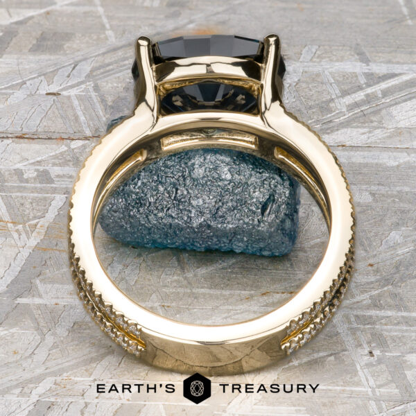 The "Gaia" ring in 14k yellow gold with 4.63-Carat Montana Sapphire The "Gaia" ring in 14k yellow gold, featuring a 4.63-carat Montana Sapphire, stands upright on rough gray stone, with the Earth's Treasury logo at the bottom of the image.