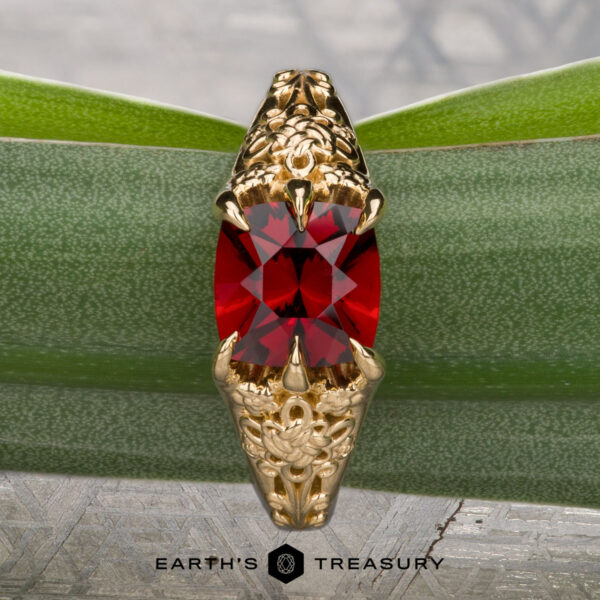 The "Guanyin" ring in 18K yellow gold with 1.94-carat Malaia garnet The "Guanyin" ring in 18K yellow gold, featuring a 1.94-carat Malaia garnet, is displayed on dark stone with a geometric patterned background.