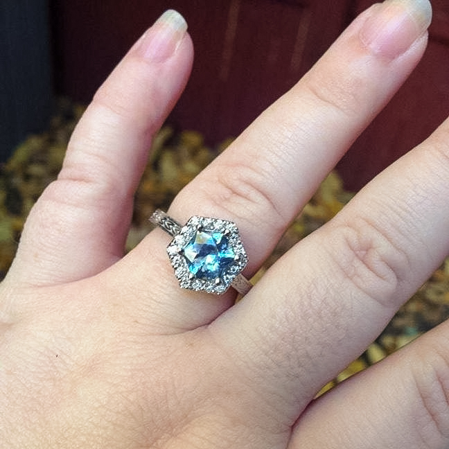 A hand wearing the KG Testimonial-1200, a hexagonal aquamarine ring accented with diamonds on the ring finger.