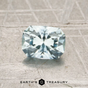 The rectangular, faceted 0.91-carat Pale Aqua Montana Sapphire (MS7192) is shown on a textured light gray surface with "EARTH'S TREASURY" and a logo displayed below.