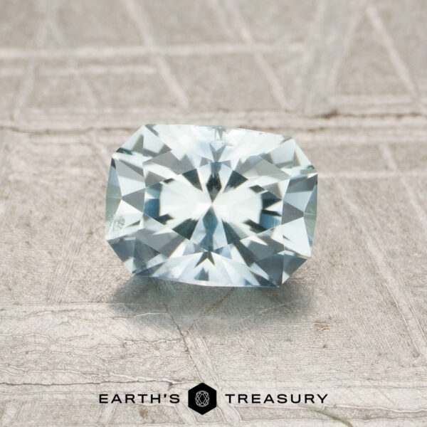 0.91-Carat Montana Sapphire (Heated) The rectangular, faceted 0.91-carat Pale Aqua Montana Sapphire (MS7192) is shown on a textured light gray surface with "EARTH'S TREASURY" and a logo displayed below.