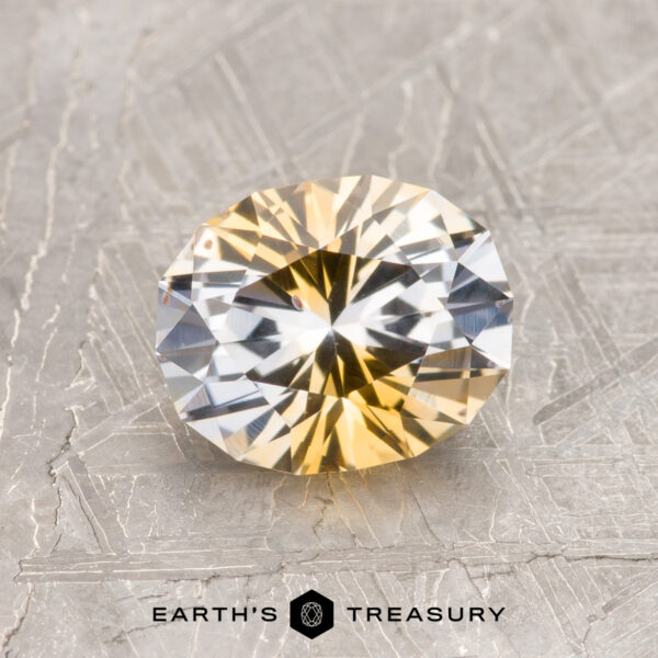 1.39-Carat Yellow-Colorless Particolored Montana Sapphire (Heated) A 1.39-carat yellow-colorless particolored Montana Sapphire (heated) is displayed on a textured gray surface, with "EARTH'S TREASURY" text and logo below.