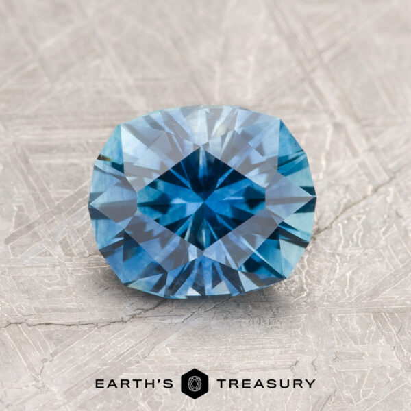 1.67-Carat Medium Blue Montana Sapphire (Heated) A 1.67-carat medium blue Montana Sapphire (heated) is displayed on a textured gray surface with the text "Earth's Treasury" and a hexagon logo beneath it.