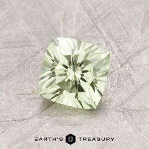 A 1.35-carat mint garnet, cut in a square shape and featuring a pale green hue, is displayed on a textured surface with the words "Earth's Treasury" visible beneath it.