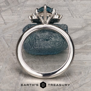 The Stacked from 55 images. Method=B (R=1,S=1) ring with a large blue gemstone is displayed upright against a rough blue stone on a textured gray surface, with the Earth’s Treasury logo at the bottom.