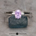 The "Fleur" ring in 14K white gold, featuring a 1.06-carat faceted Umba sapphire, is displayed upright on a blue-green stone, with the "Earth's Treasury" logo and text below.