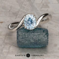 The "Minna" ring in 14K white gold featuring a 1.07-carat Montana sapphire sits on a rough blue stone atop a textured gray surface, with the "Earth's Treasury" logo displayed below.