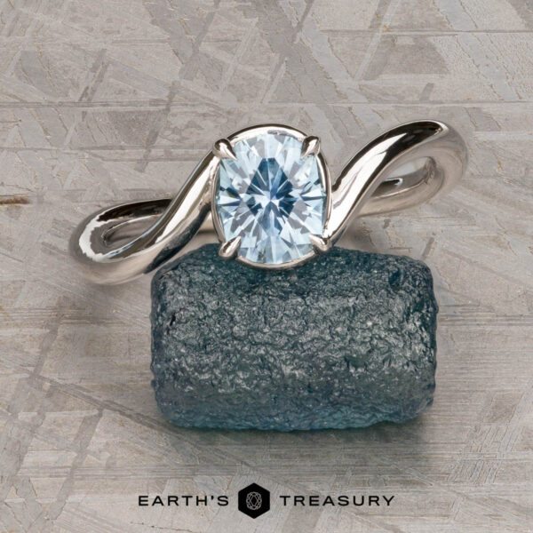 The "Minna" ring in 14K white gold with 1.07-carat Montana sapphire The "Minna" ring in 14K white gold featuring a 1.07-carat Montana sapphire sits on a rough blue stone atop a textured gray surface, with the "Earth's Treasury" logo displayed below.
