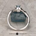 The "Minna" ring in 14K white gold featuring a 1.07-carat Montana sapphire sits on a rough blue stone atop a textured gray surface, with the "Earth's Treasury" logo displayed below.