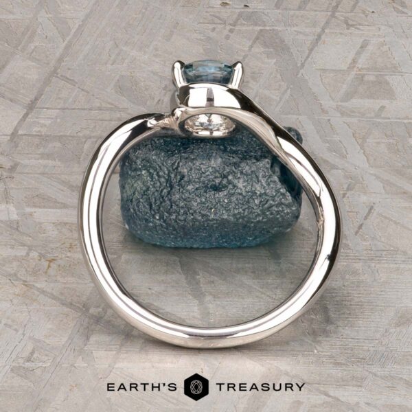 The "Minna" ring in 14K white gold with 1.07-carat Montana sapphire The "Minna" ring in 14K white gold featuring a 1.07-carat Montana sapphire sits on a rough blue stone atop a textured gray surface, with the "Earth's Treasury" logo displayed below.