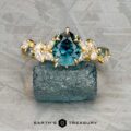 The "Posey" ring in 18K yellow gold with a 1.42-carat Montana sapphire is displayed on a rough blue crystal, accented by clear marquise stones. The Earth's Treasury logo appears at the bottom.
