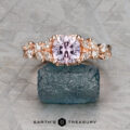 The "Posey" ring in 14k rose gold, featuring a 1.38-carat Montana sapphire, is showcased on a rough blue-green stone with the "Earth's Treasury" logo beneath.