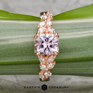 The "Posey" ring in 14k rose gold features a 1.38-carat Montana sapphire center gemstone with marquise-shaped white side stones, displayed on a green leaf with the Earth’s Treasury logo below.