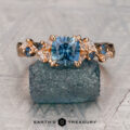 The Jiang, Xunmin (Albert) 1 ring gleams atop a rough blue mineral, its gold band crowned with a large blue gemstone center and flanked by smaller blue and clear stones.