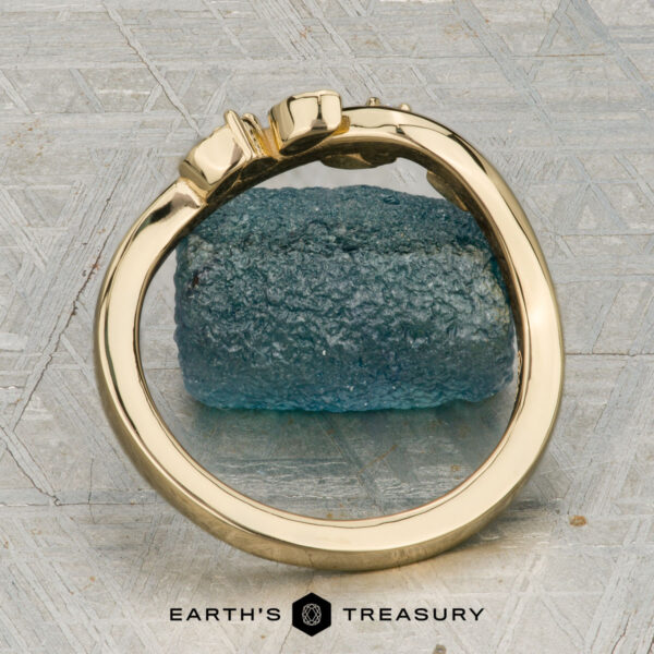 The "Ivey" band in 18K yellow gold The "Ivey" band in 18K yellow gold features a twisted design with delicate leaf accents and two sparkling diamonds, shown resting on a rough blue crystal.