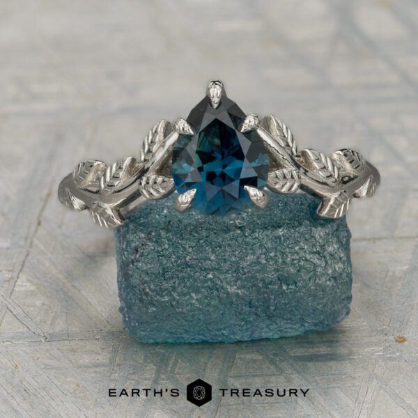 The "Ivey" ring in platinum with 1.12-carat Montana sapphire The "Ivey" ring in platinum, featuring a 1.12-carat Montana sapphire and leaf design, is displayed on textured blue stone with "EARTH'S TREASURY" text at the bottom.