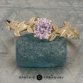 The “Ivey” ring in 14K yellow gold, featuring a 0.82-carat Montana sapphire and leaf design, is displayed on a rough blue-green stone with the "EARTH'S TREASURY" logo and text below.