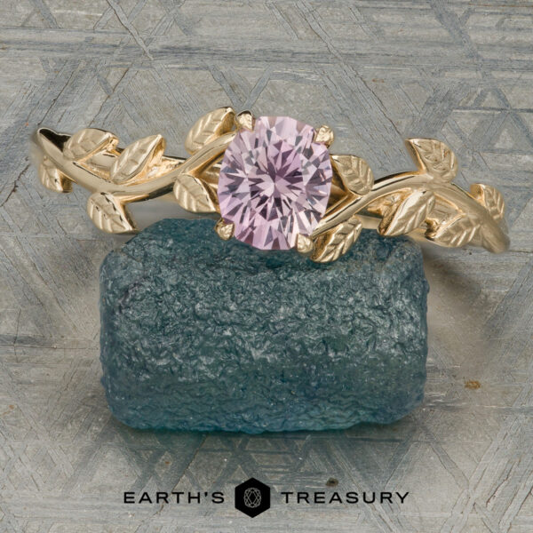 The “Ivey” ring in 14K yellow gold with 0.82-carat Montana sapphire The “Ivey” ring in 14K yellow gold, featuring a 0.82-carat Montana sapphire and leaf design, is displayed on a rough blue-green stone with the "EARTH'S TREASURY" logo and text below.