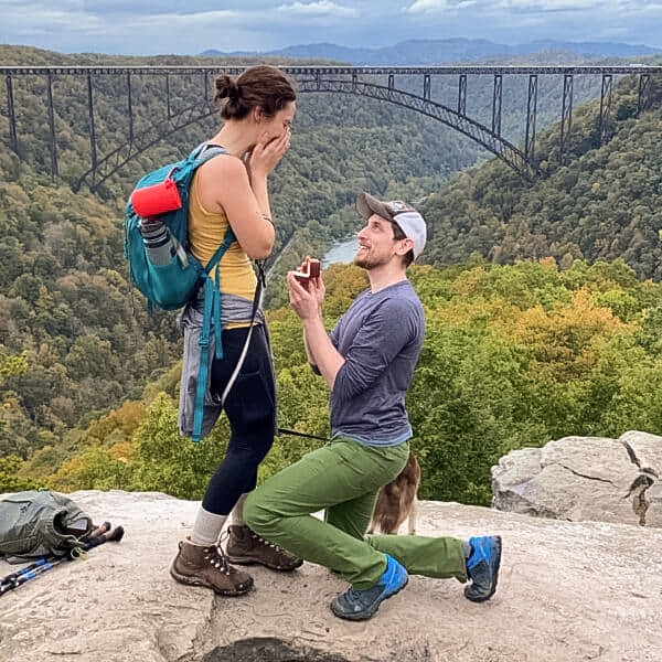 A photo from a customer review of a couple in hiking gear on a cliff overlooking scenic forest and river