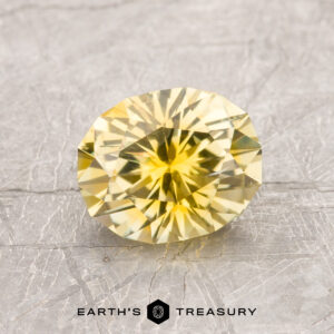 A 1.66-carat Bright Yellow Montana Sapphire (heated, oval-cut) is shown on a textured gray surface with the "Earth's Treasury" logo beneath it.