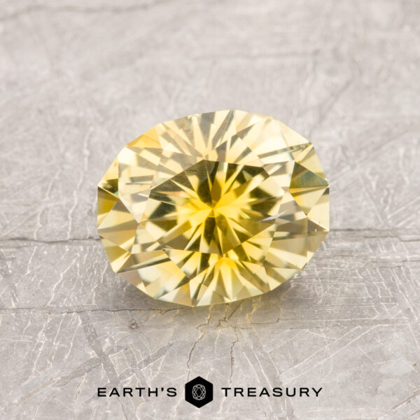 1.66-Carat Bright Yellow Montana Sapphire (Heated) A 1.66-carat Bright Yellow Montana Sapphire (heated, oval-cut) is shown on a textured gray surface with the "Earth's Treasury" logo beneath it.