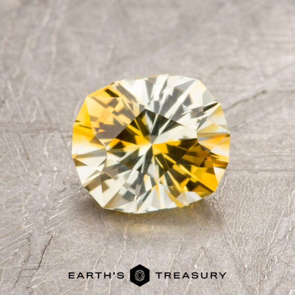 1.40-Carat Yellow-Gold Particolored Montana Sapphire (Heated) A 1.40-carat Yellow-Gold Particolored Montana Sapphire (Heated) with intricate faceting rests on a textured surface, featuring the Earth's Treasury logo and name at the bottom.