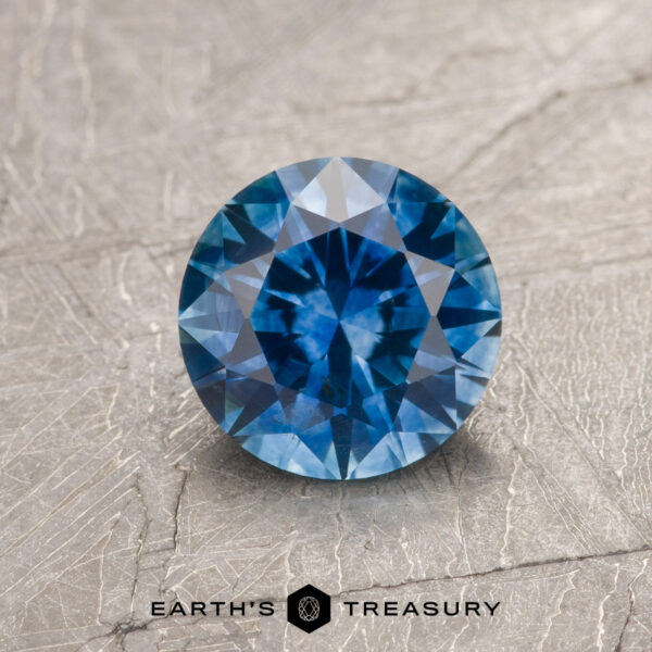 1.29-Carat Medium Blue Montana Sapphire (Heated) A 1.29-carat medium blue Montana sapphire (heated) is displayed on a textured gray surface, with the text "EARTH'S TREASURY" at the bottom.