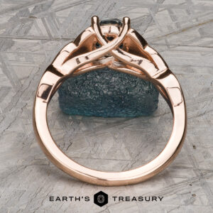 The "Aislinn" ring in 14k rose gold features a 1.69-carat Montana sapphire and an intricate band, standing upright on a textured grey background with the Earth's Treasury logo at the bottom.