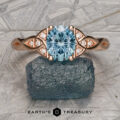 Stacked from 53 images (Method=B, R=1, S=3), the rose gold Aislinn Ring with an oval aquamarine center and diamond accents is shown on a rough blue mineral, set against a geometric background.