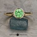 The "Emma" ring in 14k yellow gold with a 1.49-carat Tsavorite Garnet and wave texture band rests on a rough, dark blue stone with the text "EARTH'S TREASURY" below.