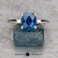 The "Finella" ring in platinum features a 2.13-carat Montana sapphire center stone flanked by two clear stones, displayed on rough blue crystal with the "Earth's Treasury" logo below.