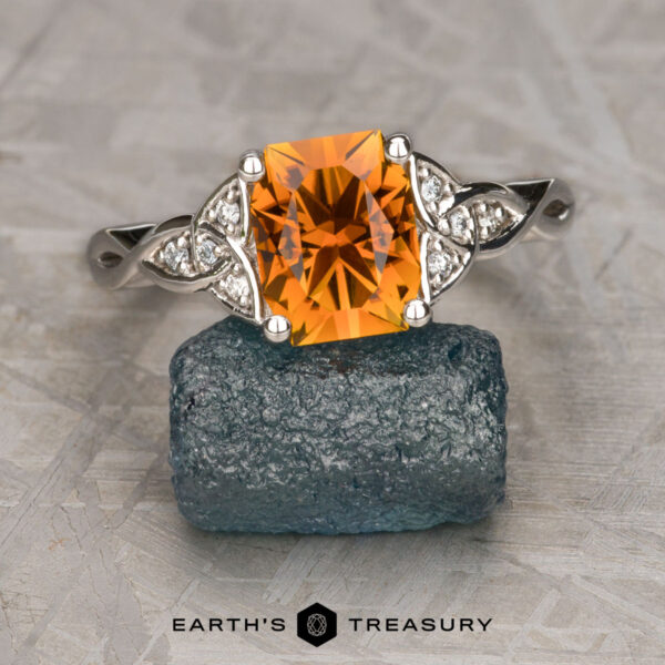 The "Aislinn" ring in 14K white gold with 2.37-carat tourmaline The "Aislinn" ring in 14K white gold, showcasing a 2.37-carat tourmaline, is elegantly displayed on rough blue-green crystal with the "Earth's Treasury" logo below.