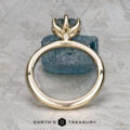 The Minimal "Anemone" ring in 14k yellow gold with a 1.46-carat Montana sapphire is showcased solitaire atop a rough blue crystal, against a textured gray background. The text "EARTH'S TREASURY" appears below.