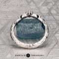 The "Magnolia" band in platinum, featuring three marquise and pear-cut gemstones, rests on a rough blue crystal with a geometric patterned background and the “Earth’s Treasury” logo below.