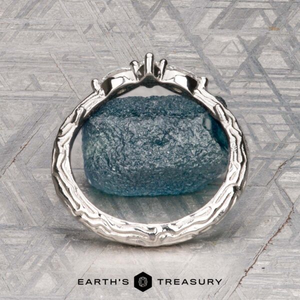 The "Magnolia" band in platinum The "Magnolia" band in platinum, featuring three marquise and pear-cut gemstones, rests on a rough blue crystal with a geometric patterned background and the “Earth’s Treasury” logo below.