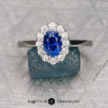 The "Elaine" ring in platinum, featuring a 1.44-carat Ceylon sapphire surrounded by accent stones, is displayed on a textured blue block with "Earth's Treasury" text below.